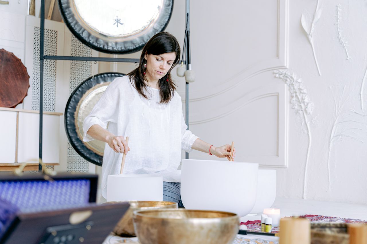 A woman uses singing bowls and gongs for a soothing sound healing therapy session indoors.