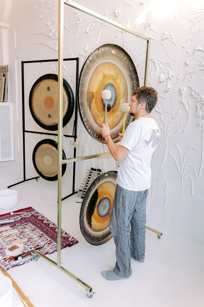 Adult male performing meditation with gongs for sound healing indoors.