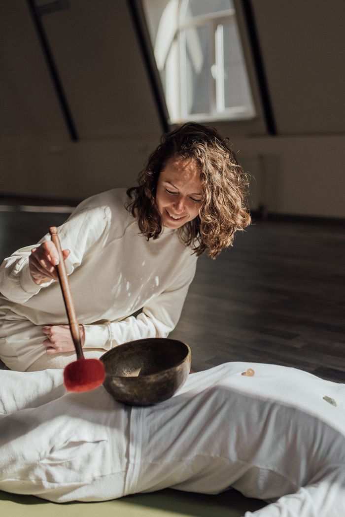 Woman using a Tibetan singing bowl during a relaxing sound therapy session indoors.